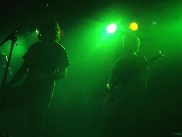 A band on stage under heavy green light, two players silhouetted against the haze.