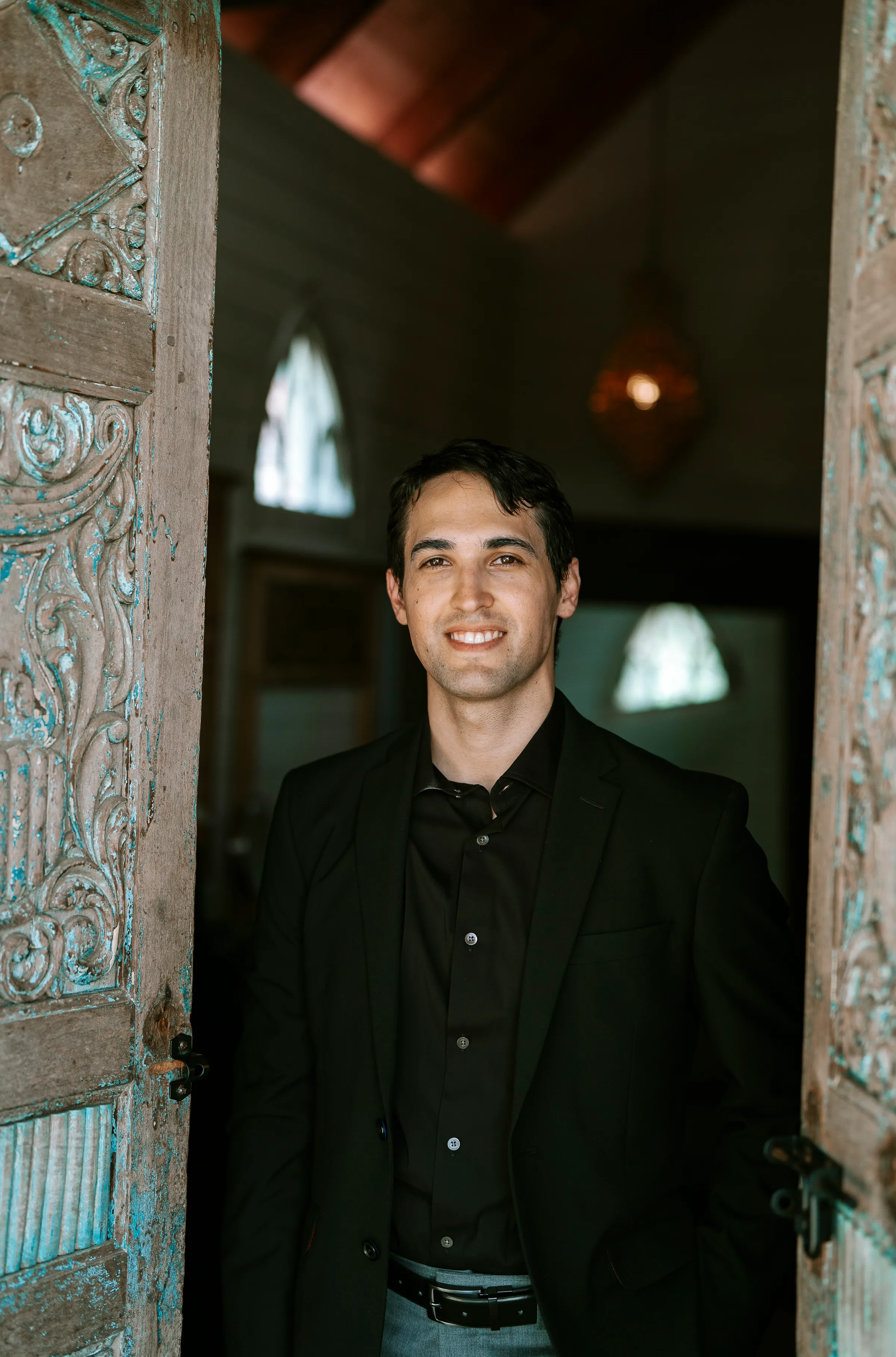 Jordan Burkland, in a dark shirt, standing in an ornate doorway under warm low light.
